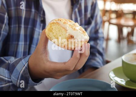 Gros plan de la main masculine mangeant un beignet sucré dans le café Banque D'Images
