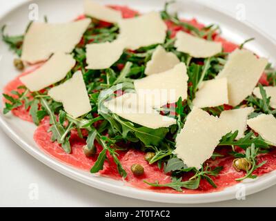 Apéritif froid carpaccio de boeuf avec parmesan, câpres et roquette sur plaque blanche vue rapprochée extrême Banque D'Images