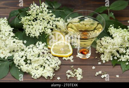 verre original avec liqueur de fleur de sureau avec décoration de fleurs âgées sur fond en bois Banque D'Images