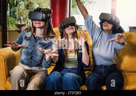 Trois jeunes femmes, deux caucasiennes et une brésilienne, assises sur un canapé, ont vécu une expérience de réalité augmentée 360° 3D, en faisant des gestes de la main avec V. Banque D'Images