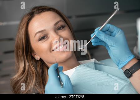 Patient dans un fauteuil dentaire regardant la caméra et souriant. Belle et jolie femme. Mains avec des instruments chez un dentiste diagnostiquant un patient dans un Banque D'Images