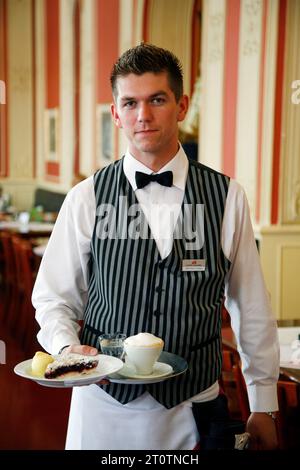 Serveur tenant un café et un gâteau au café Louvre dans Narodni Trida 2 rue, Nove Mesto, Prague, République tchèque. Banque D'Images