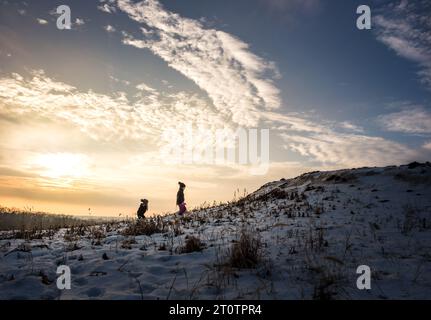 Sœurs marchant jusqu'à la colline enneigée au coucher du soleil Banque D'Images