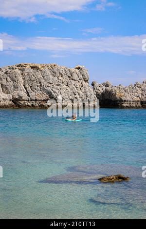 Homme célibataire assis sur une planche de surf bleu sarcelle dans l'eau de la plage de Saint Paul's Bay Banque D'Images
