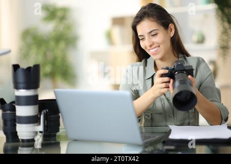 Heureux photographe vérifiant le travail sur ordinateur portable tenant l'appareil photo à la maison Banque D'Images