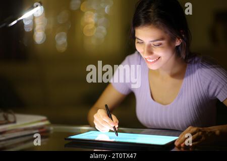 Femme heureuse à l'aide du stylet dans la tablette dans la nuit à la maison Banque D'Images