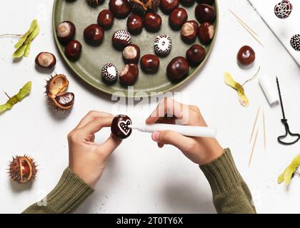 Étape 4. Peignez un cœur sur une châtaigne avec un peintre acrylique blanc. Faire décor d'automne pour Holliday avec des enfants. Vue de dessus. Banque D'Images