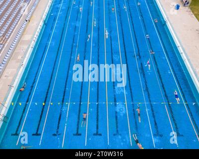 La piscine sportive ouverte brillait sous le soleil éclatant tandis que les gens nageaient dans ses eaux accueillantes. Leurs traits synchronisés ont créé un t vibrant Banque D'Images