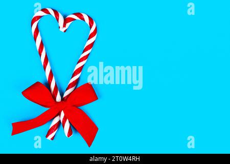 Vue supérieure de la canne de Noël à rayures de couleurs de Noël en forme de cœur avec arc rouge sur fond bleu. Libre. Noël, fêtes de fin d'année. copier l'espace. Banque D'Images
