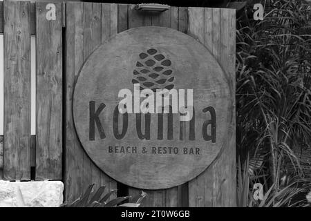 Panneau logo en bois Kounna Beach et Resto Bar à l'entrée du restaurant Anthony Quinn Bay en bord de mer en noir et blanc Banque D'Images