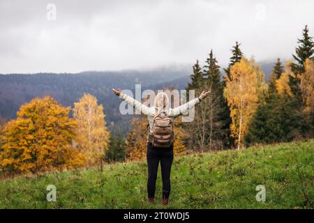 Femme avec sac à dos profitant de la vue sur la forêt d'automne pendant la randonnée dans les montagnes. Des gens en harmonie avec la nature Banque D'Images