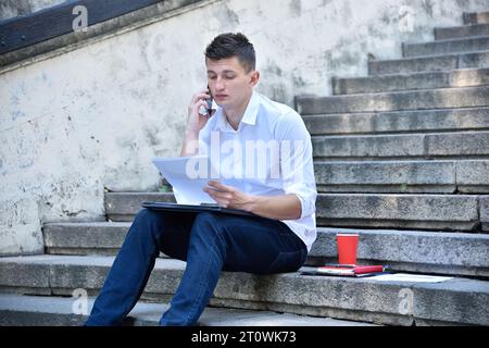 Jeune homme d'affaires assis sur l'escalier et parlant avec un collègue au téléphone. Concept de commerce et de communication. Banque D'Images