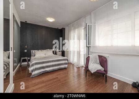 Chambre double en suite, commode avec tiroirs blancs, TV attachée au mur, balcon avec aluminium et porte en verre, fauteuil rembourré en v Banque D'Images