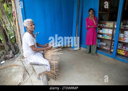 Homme local devant un mur en bois de couleur bleue faisant des paniers tissés à la main, île de Majuli, rivière Brahmapoutre, Assam, Inde Banque D'Images