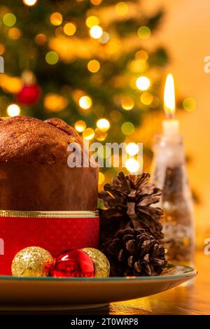 Goiânia, Goias, Brésil – 08 octobre 2023 : un panettone, des pommes de pin, des bougies allumées, des boules et un sapin de Noël en arrière-plan avec des lumières bokeh. Banque D'Images