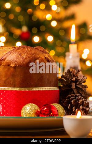 Goiânia, Goias, Brésil – 08 octobre 2023 : un panettone, des pommes de pin, des bougies allumées, des boules et un sapin de Noël en arrière-plan avec des lumières bokeh. Banque D'Images