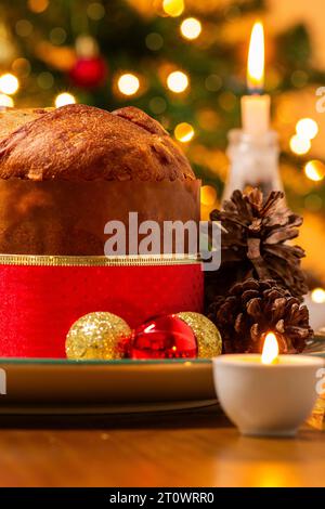 Goiânia, Goias, Brésil – 08 octobre 2023 : un panettone, des pommes de pin, des bougies allumées, des boules et un sapin de Noël en arrière-plan avec des lumières bokeh. Banque D'Images