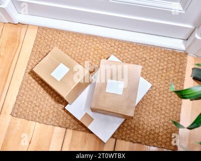 Pile de colis en carton livrés sur un tapis de porte à côté de l'entrée de l'appartement Banque D'Images