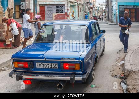 Une voiture Lada conduite dans une rue de la ville par des Cubains qui sont dans leur mode de vie normal. Le trottoir est cassé et sale. Les bâtiments sont altérés a Banque D'Images