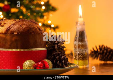 Goiânia, Goias, Brésil – 08 octobre 2023 : un panettone, des pommes de pin, des bougies allumées, des boules et un sapin de Noël en arrière-plan avec des lumières bokeh. Banque D'Images