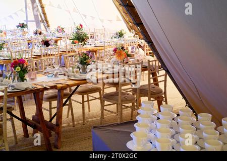 Chapiteau de mariage décoré et prêt pour les invités à arriver. Tables, chaises, fleurs et décors. Une conception rustique de tipi de tente. Banque D'Images