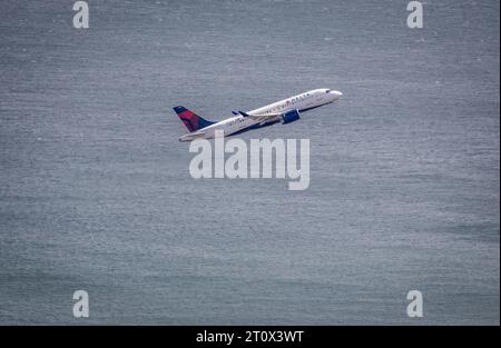 Un avion commercial moderne est vu dans le ciel alors qu'il passe au-dessus des eaux bleues sereines d'une plage côtière Banque D'Images