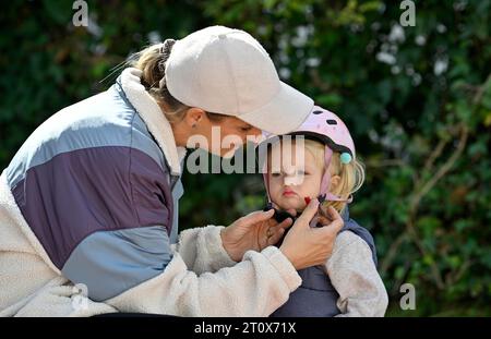 Mère, femme, blonde, casquette de baseball, met sur petite fille, 2 ans, blonde, casque, rose, ferme la charnière, Stuttgart, Baden-Wuerttemberg, Allemagne Banque D'Images