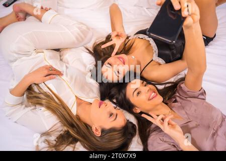 Style de vie des amis caucasiens en vacances dans un hôtel au lit, photographié d'en haut, prenant un selfie avec le téléphone Banque D'Images