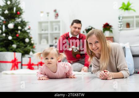 La famille heureuse séjourne dans une chambre près d'un sapin de Noël décoré et de cadeaux Banque D'Images