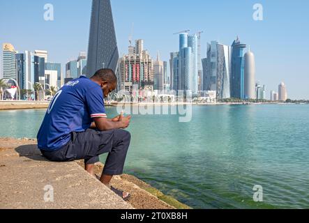 L'homme est assis sur les marches de la Corniche avec des gratte-ciel en arrière-plan, West Bay, Doha, Qatar Banque D'Images