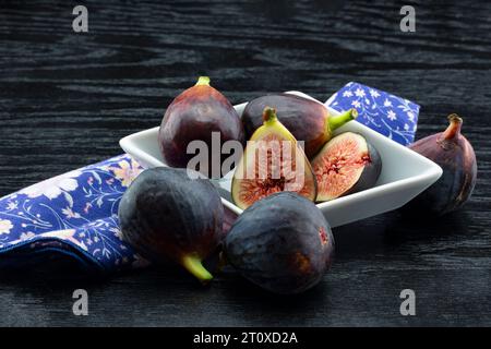 Nature morte décontractée de figues coupées et entières dans le plat et sur la serviette, le tout sur fond sombre et rustique de planche de bois noir Banque D'Images