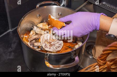 Vue rapprochée des mains féminines dans des gants en caoutchouc nettoyant les champignons dans l'évier de cuisine. Banque D'Images