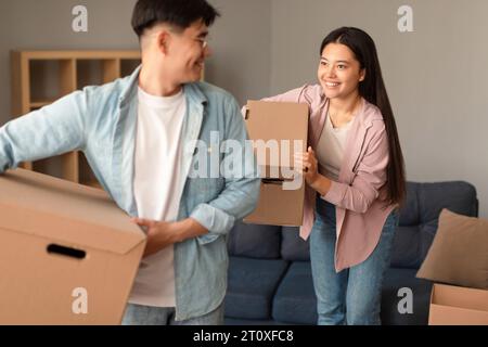 Joyeux époux coréens se déplaçant transportant des boîtes en carton quittant l'appartement Banque D'Images