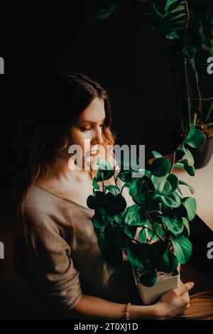 Une jeune femme belle et délicate assise avec une plante luxuriante et verte dans ses mains. Il symbolise son amour pour la nature et les plantes, mettant en valeur des thèmes Banque D'Images