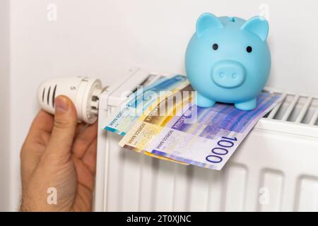 Coûts de chauffage des appartements en hiver en Norvège, concept énergétique et économique, dévissage à la main du radiateur, tirelire et un paquet de couronnes norvégiennes Banque D'Images