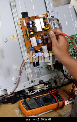 Le Caire, Egypte, octobre 3 2023 : un ingénieur technicien utilisant un multimètre numérique, le circuit d'alimentation de la carte principale de télévision LCD, des fils, des transformateurs, des résis Banque D'Images