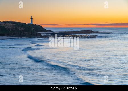 Paysage marin du lever du soleil avec une banque de nuages basse et le phare de Norah Head de Soldiers Beach sur la côte centrale, Nouvelle-Galles du Sud, Australie. Banque D'Images