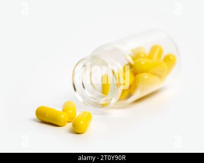 Pilules jaunes près de la bouteille en verre ouverte couchée isolée sur fond blanc. Concept de traitement médical avec des médicaments, des vitamines ou des suppléments dans Banque D'Images