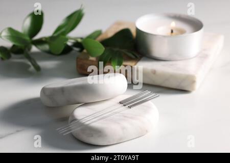 Pierres avec des aiguilles d'acupuncture sur la table blanche Banque D'Images