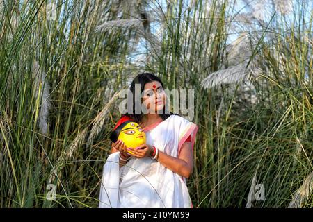 La mannequin Rima Bhattacharya pose en portant un saree indien traditionnel et tenant un visage d'argile d'idole Durga pendant la séance photo en plein air Agomoni concept dans une zone remplie de chatons ou de cachous à environ 60 km de Kolkata. Le mannequin Rima Bhattacharya pose pour une photo pour la série photo basée sur le thème de Durga Puja Vibes en Inde. Rima Bhattacharya, mannequin de mode et célébrité dans l'industrie de la mode et de la télévision bengali collabore avec la série photo pour promouvoir Durga Puja. La série photo est organisée par un groupe de photographes visant à documenter et promouvoir la pré- Banque D'Images