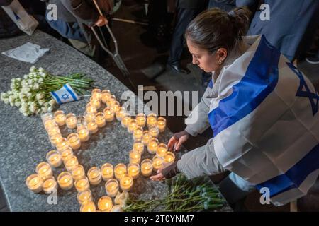 New York, États-Unis. 09 octobre 2023. Une femme drapée de drapeau israélien s'occupe du mémorial de fortune fait de bougies commémoratives en forme de début de David et de fleurs lors d'une veillée aux chandelles pour les victimes d'attaques terroristes en Israël sur la place Golda Meir de Manhattan le 9 octobre 2023 à New York. Le 7 octobre, le groupe militant palestinien Hamas a lancé une attaque surprise contre Israël depuis Gaza par terre, mer et air, tuant plus de 900 personnes et en blessant plus de 2000. Selon certaines informations, 130 soldats et civils israéliens ont également été enlevés par le Hamas et emmenés à Gaza. Crédit : Banque D'Images