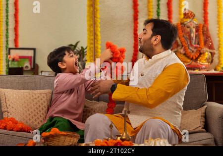 Père et fils garnissant des fleurs ensemble à la maison à l'occasion de Ganesh Chaturthi Banque D'Images