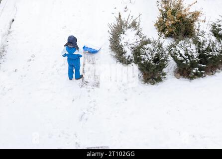 garçon dans un hiver chaud avec une grande pelle aide à dégager la neige de la cour après une tempête de neige. Hiver, mauvais temps, froid, aide de la mère Banque D'Images