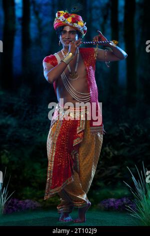 Jeune homme déguisé en Seigneur Krishna et jouant de la flûte à l’occasion de Janmashtami Banque D'Images