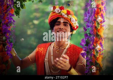 Jeune homme déguisé en Seigneur Krishna et assis sur une balançoire à l’occasion de Janmashtami Banque D'Images