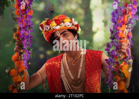 Jeune homme déguisé en Seigneur Krishna et assis sur une balançoire à l’occasion de Janmashtami Banque D'Images