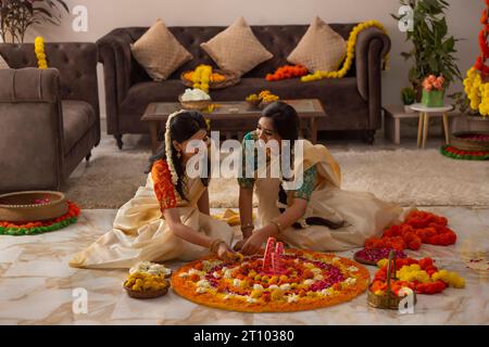 Femmes du sud de l'Inde en saree blanc décorant le sol avec des fleurs pour célébrer Onam Banque D'Images