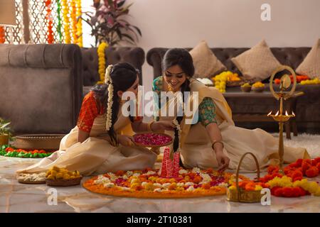 Femmes du sud de l'Inde en saree blanc décorant le sol avec des fleurs pour célébrer Onam Banque D'Images