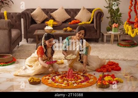 Femmes du sud de l'Inde en saree blanc décorant le sol avec des fleurs pour célébrer Onam Banque D'Images