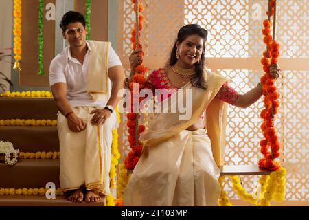 Femme souriante assise sur un swig sur Onam tandis que son mari assis derrière Banque D'Images